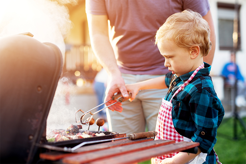 Young boy grilling food on bbq with father