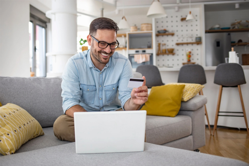 Happy man with eye glasses holding credit card while working on laptop