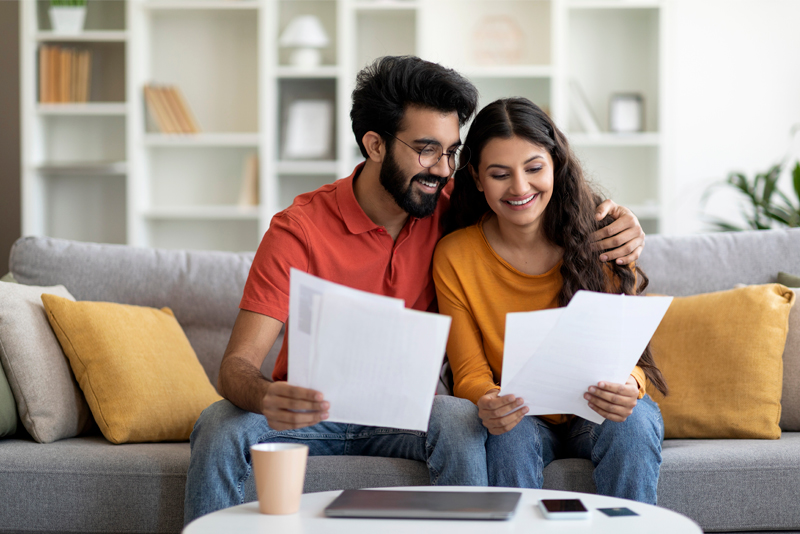Happy couple looking at paperwork while sitting on living room couch